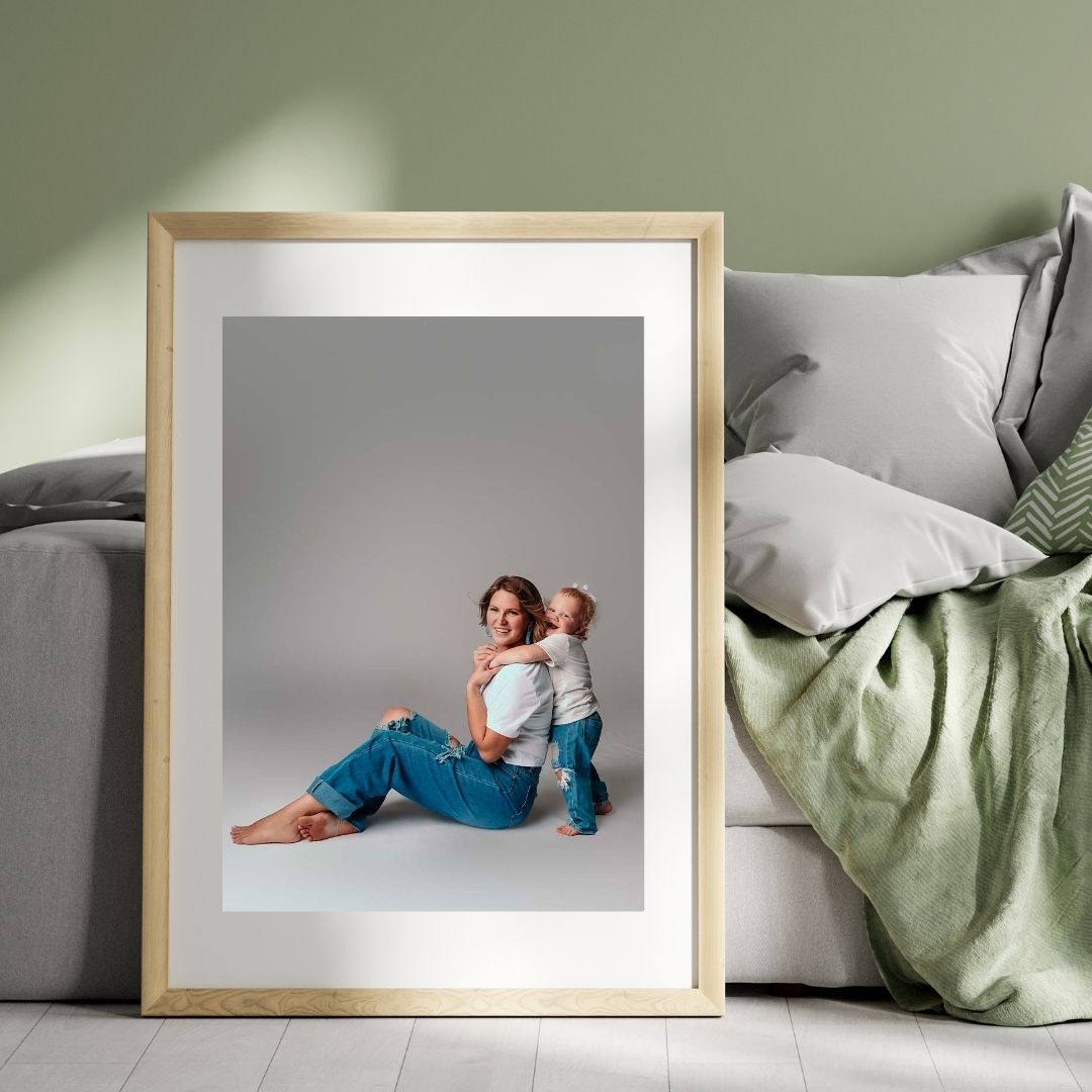 A digital mockup of a motherhood portraits featuring a young mom, playing with her toddler daughter. They are wearing matching blue jeans and white t shirts, and are visibly joyful to be together. Photography by Mobile, AL famlily photographer on a white backdrop.
