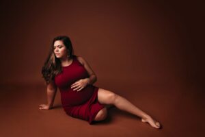An expecting mom in a red dress, posing for a maternity portrait before she begins prepping her hospital bag using the hospital back checklist provided by Mobile, AL Maternity Photographer