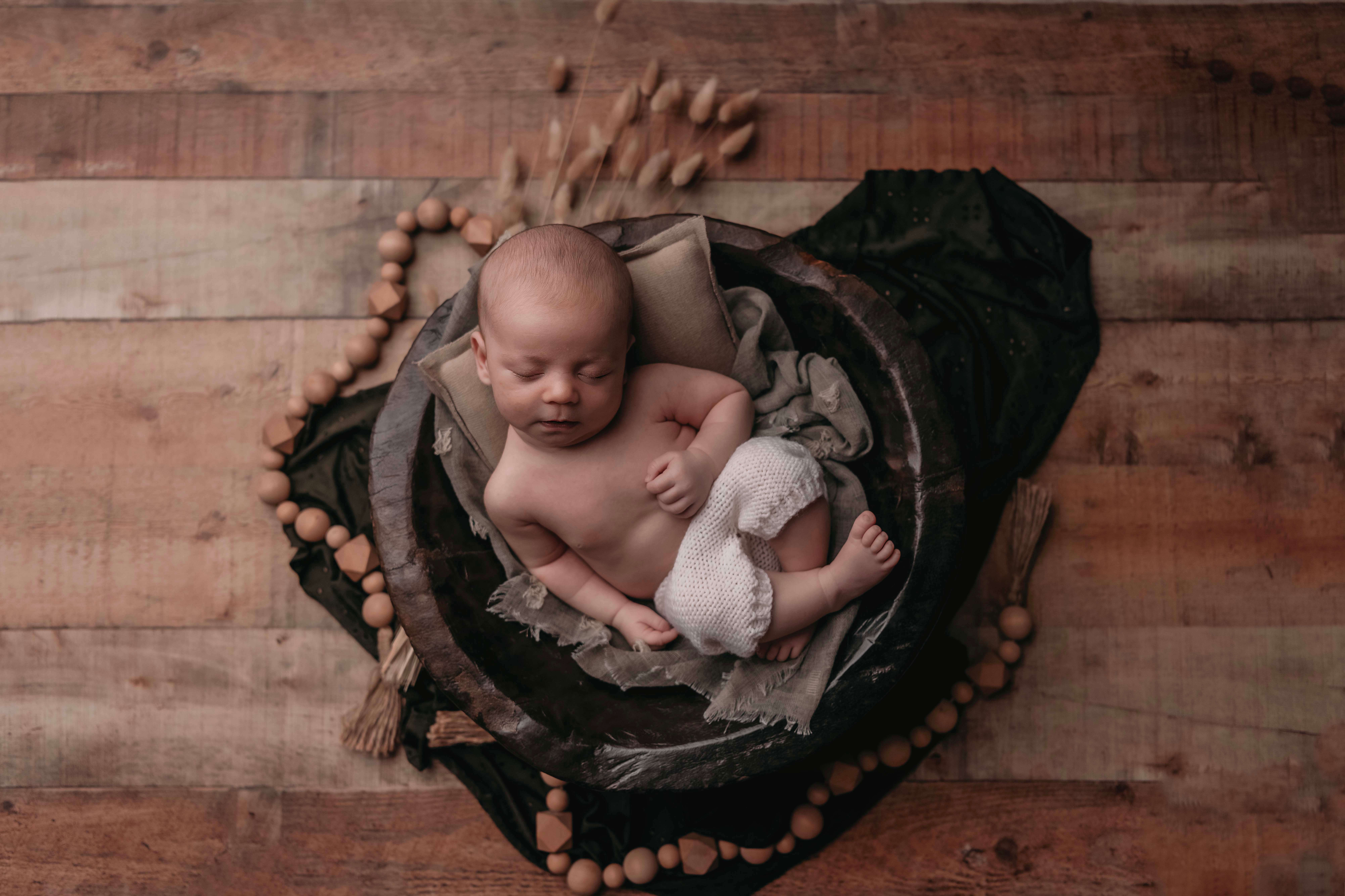 A newborn photo of a baby boy in a basket that is laying on a wood floor