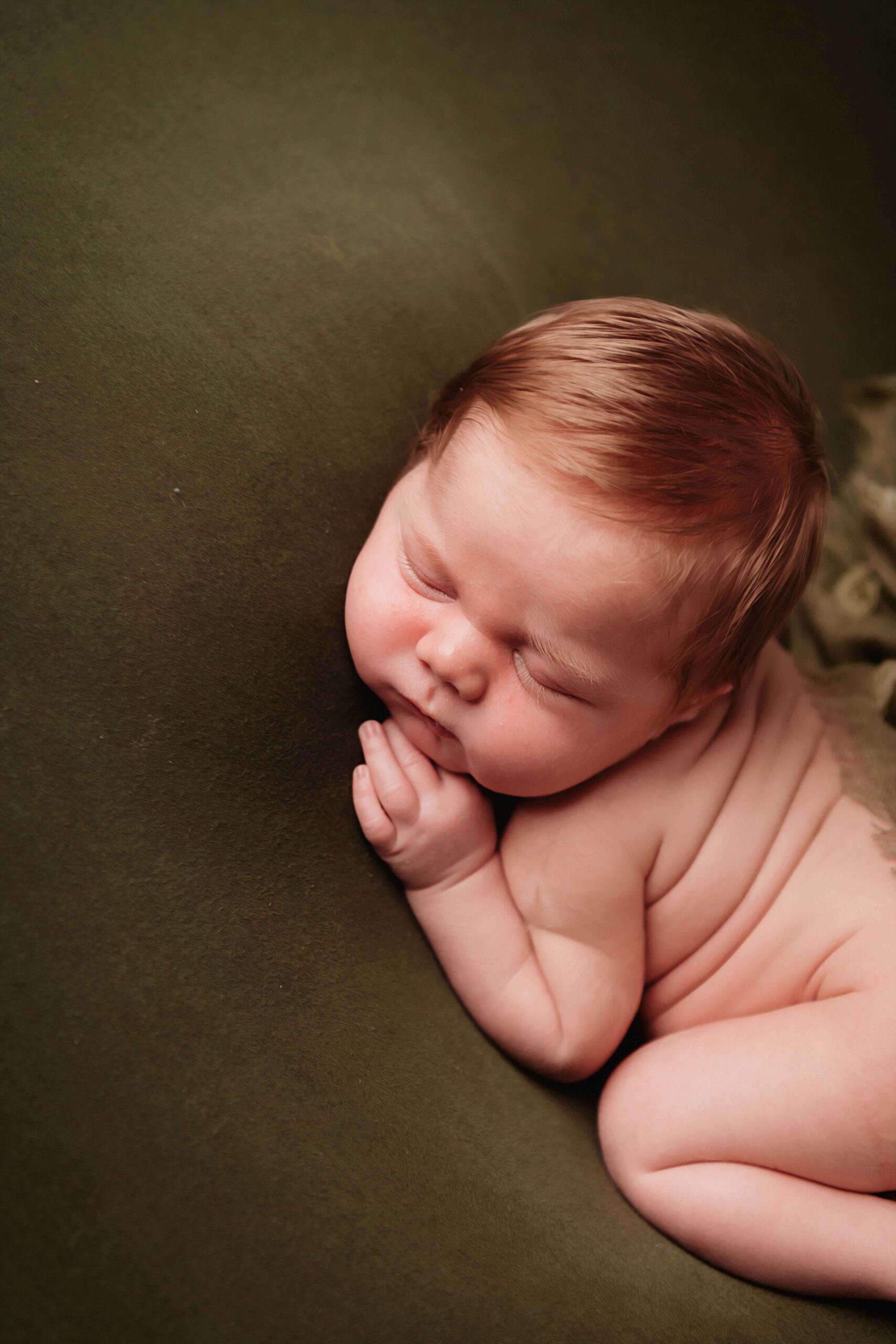 A baby sleeping soundly on a green backdrop, photographed by Mobile AL Newborn photographer